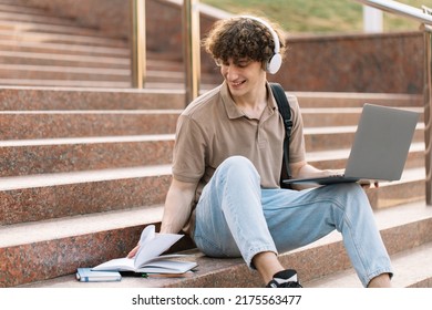Concept of e-learning, distance study or remote learning concept, Young happ curly hair school guy, college or university student with backpack and headphones using laptop sitting on steps