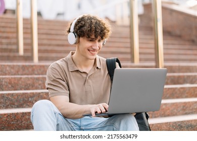 Concept Of E-learning, Distance Study Or Remote Learning Concept, Young Happy Curly Hair School Guy, College Or University Student With Backpack And Headphones Using Laptop Sitting On Steps