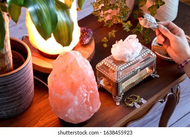 Concept Of Eliminating Negative Energy, Uplifting Your Spirit And Calming The Mind At Home. Female Holding And Clear The Bad Energy Using White Sage At Wooden Desk With Salt Lamps And Crystals.