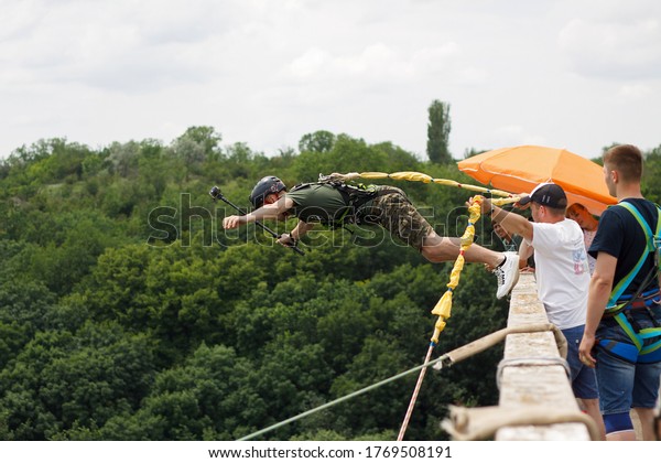 Concept of Extreme Sports and Fun. A man is a \
thrill-seeker and a  rope jumper from the bridge. He is very happy\
to make a dream come true. He  is holding an action camera and\
insanely happy