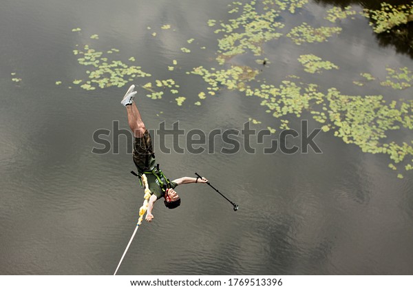 Concept of Extreme Sports and Fun. A man is a \
thrill-seeker and a  rope jumper from the bridge. He is very happy\
to make a dream come true. He  is holding an action camera and\
insanely happy