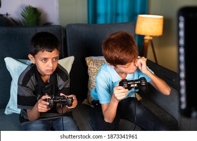 Concept Of Eye Strain Due To Over Night Video Game Play - Two Kids Playing Video Game During Late Night At Home And One Kid Rubbing His Eyes Due Eye Irritations