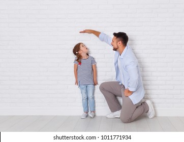 concept of the family. the father measures growth of child to a daughter near an empty wall