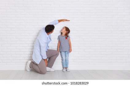 Concept Of The Family. The Father Measures Growth Of Child To A Daughter Near An Empty Wall
