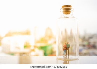 Concept Of Family Future Plan And  Insurance. Miniature People: Small Couple Lover Figures Standing Inside A Bottle With Cityscape Background And Copy Space For Text.