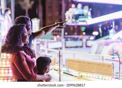 Concept Of Family And Leisure. Happy Family At Luna Park, Dad Pointing To The New Carousel.