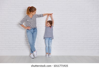 concept of the family. mother measures growth of child to a daughter near an empty wall