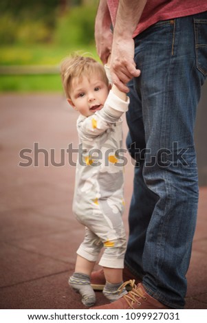 Concept: family values. Portrait of adorable innocent funny brown-eyed baby hold hands and try to stand with help of his father