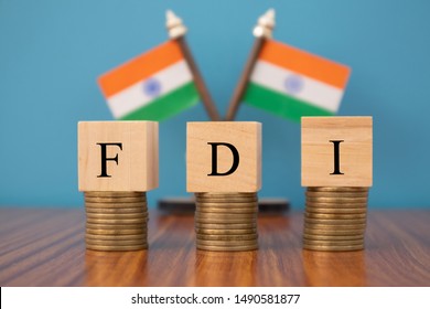 Concept Of FDI Or Foreign Direct Investment On India In Wooden Block Letters On Stack Of Coins With Indian Flag As A Background.