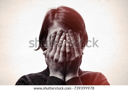 Concept of fear, shame, domestic violence. Woman covers her face her hands on light  scratched background. Black and white image.