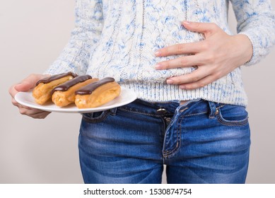 Concept of feeling bad after eating too much sweets. Cropped close up photo of woman holding crockery with three glazed eclairs isolated grey background