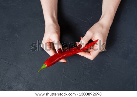 Concept: female hands holding hot chili peppers. Dark background, top view, space for text