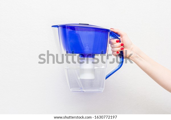 Concept of filtered clean\
water. Woman\'s hand with water filter jug, closeup, white\
background