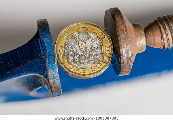 Stock Photo of a UK sterling pound coin being squeezed in a solid clamp or vice