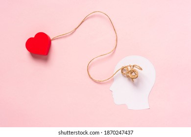 The concept of finding love. White paper silhouette of a head with tangled threads inside as an analogy to confused thoughts and a heart on a string