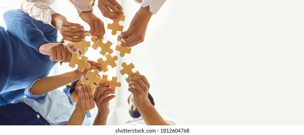 Concept of finding solution. From below of company workers assembling pieces of jigsaw puzzle in work meeting. Banner with happy office employees playing game during team building activity