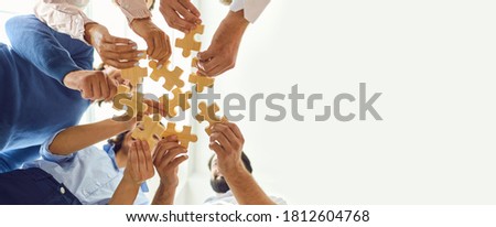 Concept of finding solution. From below of company workers assembling pieces of jigsaw puzzle in work meeting. Banner with happy office employees playing game during team building activity