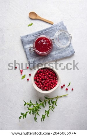 Concept flat lay with homemade lingonberry jam and forest cowberry in bowl on white table with blue napkin.  Top view and copy space image