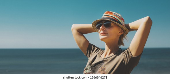 Concept Of Freedom, Happiness, Tourism, Adventure And Leisure. Attractive Middle-aged Woman In Hat, Keep Your Hands To Your Head And Enjoy Picturesque Landscape At Resort