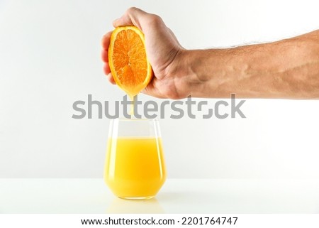 concept of freshly squeezed orange juice. hand squeezes juice from orange into a glass. fresh orange juice flowing into a glass on white background