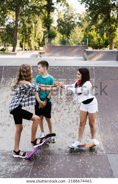 Concept\
of friendship sports support of children. Kids with skateboards and\
penny boards stack their hands together and get ready for ride\
together on sport ramp on skate board\
playground