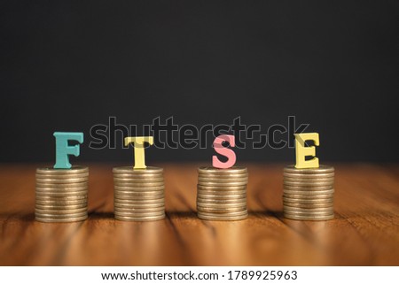 Concept of FTSE or Financial Times Stock Exchange showing with coins and letters on black background.