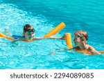 Concept of fun, health and vacation. Oudoor summer activity. Happy smiling boys eight and five years old in swim glasses swiming in the pool with noodles on hot summer day.