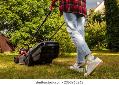 Concept of gardening, work, nature. Housework, gardening and country life. Home garden grass cutting woman mowing with lawn mower. Detail of lawn mower. Сutting grass in backyard. Sunny autumn day.