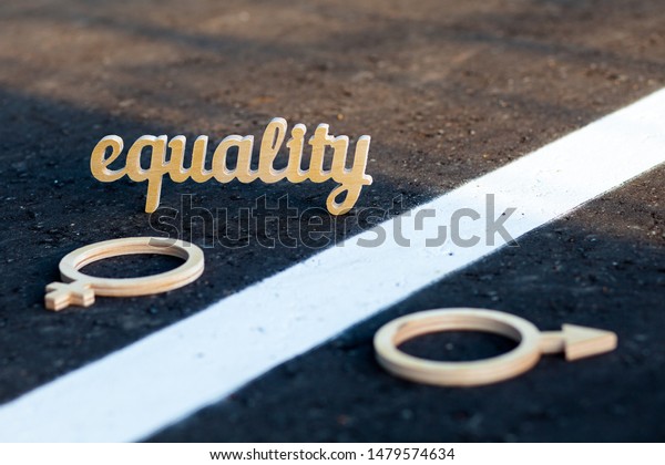 The concept of gender equality. Symbols of men
and women of plywood on the pavement. The word equality is carved
and plywood on asphalt.