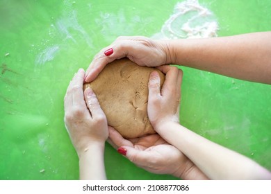 The Concept Of Generational Connection, Love And Care. Close-up Over Top View Of The Hands Of An Elderly Woman And A Girl Who Are Baking Cookies In The Kitchen And Holding The Dough In Their Hands.