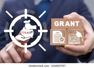 Concept Of Grants. Application Grant. Businessman Using Virtual Touchscreen And Holding Wooden Blocks With Grant Conceptual Presentation.