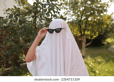 Concept of Halloween, Ghost with sunglasses. a girl in the role of a ghost runs on green grass. funny ghost in glasses