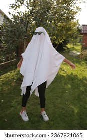 Concept of Halloween, Ghost with sunglasses. a girl in the role of a ghost runs on green grass. funny ghost in glasses