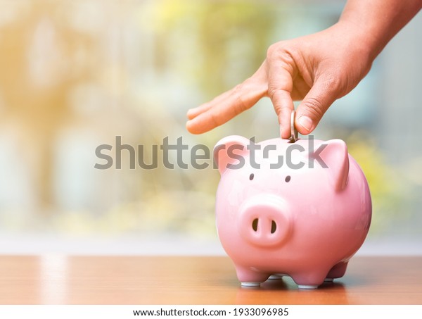 Concept hand putting money coin into piggy bank\
saving money for future plan and retirement fund, Business or\
finance saving show putting coin saving and investment money  retro\
vintage color tone.