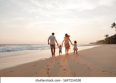 Concept of happy family. Young couple with two girls kids walking by the sea during their vacation in tropical country. Back view family enjoy sunset on the beach