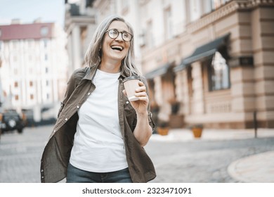 Concept of happy old age through image of silver-haired mature senior woman walking in city, enjoying cup of coffee. Woman is captured in moment of joy and contentment, with smile and positive mood - Powered by Shutterstock