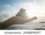 Concept of harmony, positive mind, mental health. Balance of stones on a human hand, close-up against the sea and sun. Enjoying life, balancing body, mind, soul and spirit.