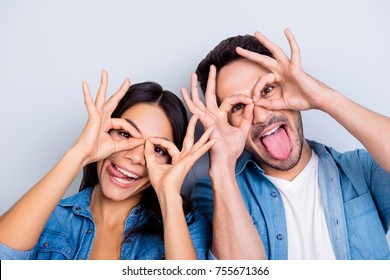 Concept of having funtime and grimacing, behaving like kids. Close up photo of two happy people making binoculars with their hands and showing tongues. Isolated on grey background