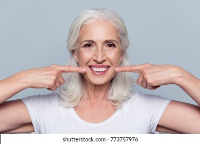 Concept of having strong healthy straight white teeth at old age. Close up portrait of happy with beaming smile female pensioner pointing on her perfect clear white teeth, isolated on gray background - Shutterstock ID 773757976