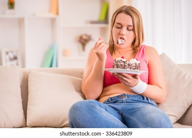 The concept of healthy eating. Fat woman eating cake sitting on the couch at home