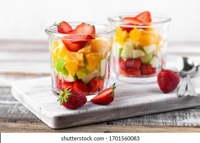 Concept Of Healthy Food, Clean Eating. Low Calories Colorful Sweet Summer Dessert. Homemade Simple Fruit Salad In Two Glasses, Ideal Breakfast. Orange, Apple, Strawberry. White Wooden Background. 