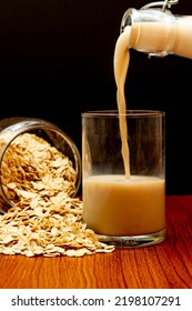 Concept Of Healthy Grain, Pour Oat Milk Into Glass And Oats Poured Out Of Jar On Wooden Background.