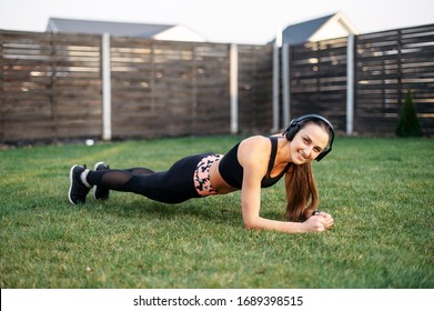Concept of a healthy lifestyle, self-discipline. A young girl in sportswear does an exercise plank on the grass outdoors