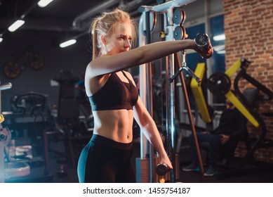 The concept of a healthy lifestyle and workouts in the gym. Blonde girl in sportswear engaged in the gym and trains with dumbbells - Shutterstock ID 1455754187
