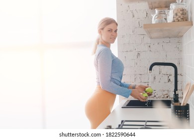 Concept Healthy Post Workout Nutrition, Vitamin Replenishment. Female In Sportswear Washes Green Apples In Kitchen Sink.