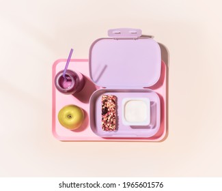The concept of healthy school meals. Food composition with lunch box with yogurt, cereal bar, apple and oatmeal berries cocktail on a pink background with window light. Flat lay, horizontal banner