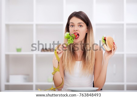 The concept of healthy and unhealthy nutrition. The model plus size makes a choice in favor of healthy food and fruit by refusing fast food and burger. XXL woman