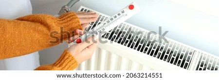 Concept of heating season with girl holds thermometer near radiator.