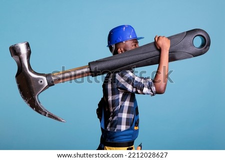 Concept of heavy work, African american builder with giant hammer in studio shot. Strong man heavy work Construction worker carrying huge work tool wearing coveralls and hard hat, construction