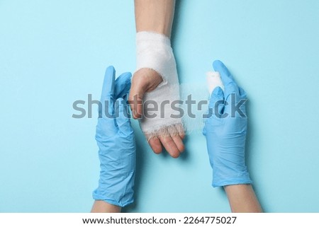 Concept of help during an injury, doctor wrapping hand in bandage on blue background